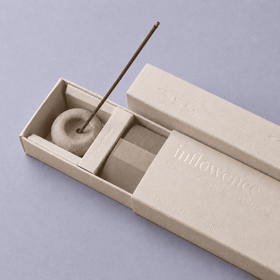 Close-up of an open inflowence incense box with a ceramic holder and a lit incense stick on a blue background.