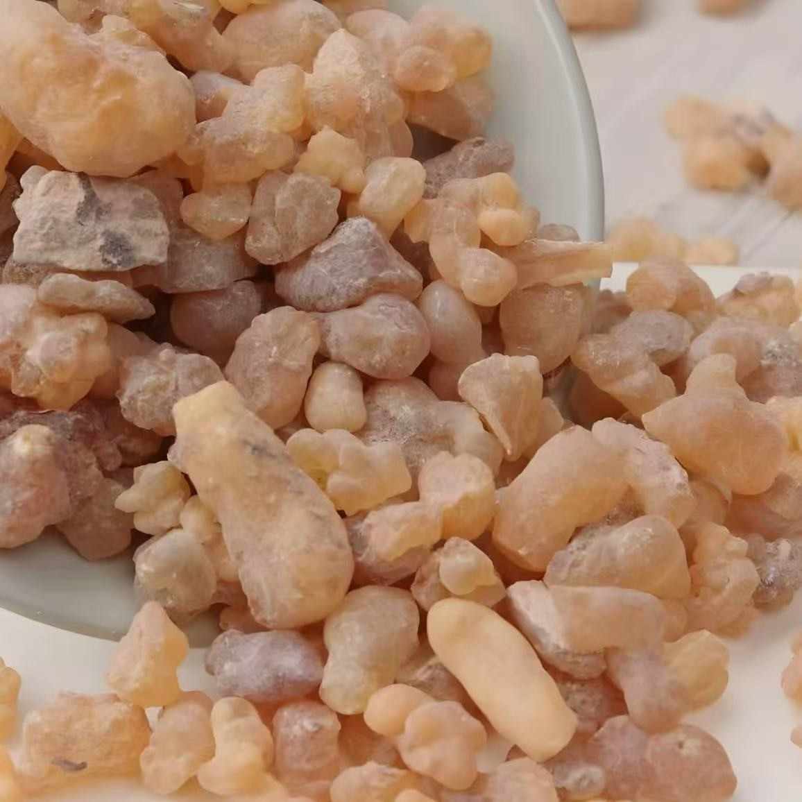 A white bowl tipped over, with light-colored frankincense resin pieces spilling out onto a white surface. The image highlights the resinous and slightly citrusy nature of the product, which promotes deep breathing and a calm, reflective mood.