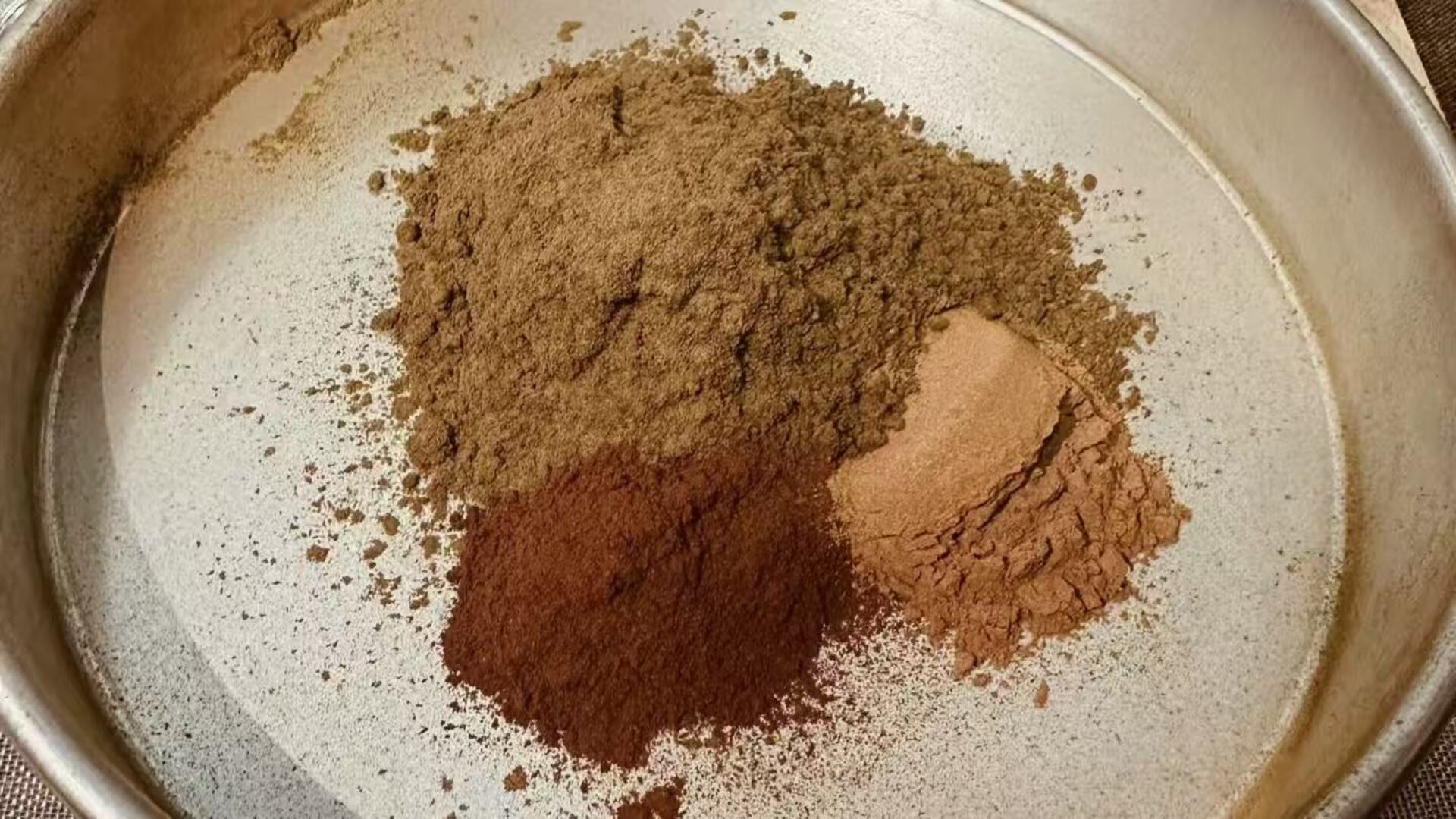 A close-up view of various brown powdered ingredients, including fragrance powders and Makko Powder, sitting in a mixing pan, illustrating the first step in the DIY guide on how to make incense at home.