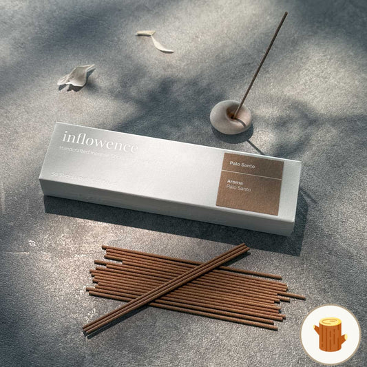 inflowence handcrafted Palo Santo incense sticks and holder on a textured stone surface with scattered petals and soft dappled light — a serene setup for meditation, intention setting, and grounding rituals.