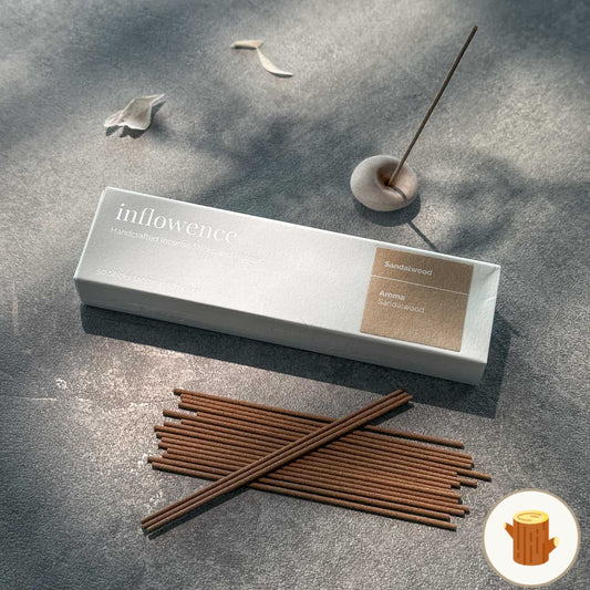 Inflowence Sandalwood incense box with neatly arranged incense sticks and a lit stick in a minimalist clay holder on a stone surface—crafted for calming, grounding rituals to center the mind and body.