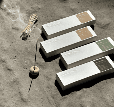A close-up view of high quality incense from inflowence next to its packaging, highlighting the sleek design and a small wooden incense holder for the best smelling incense experience.