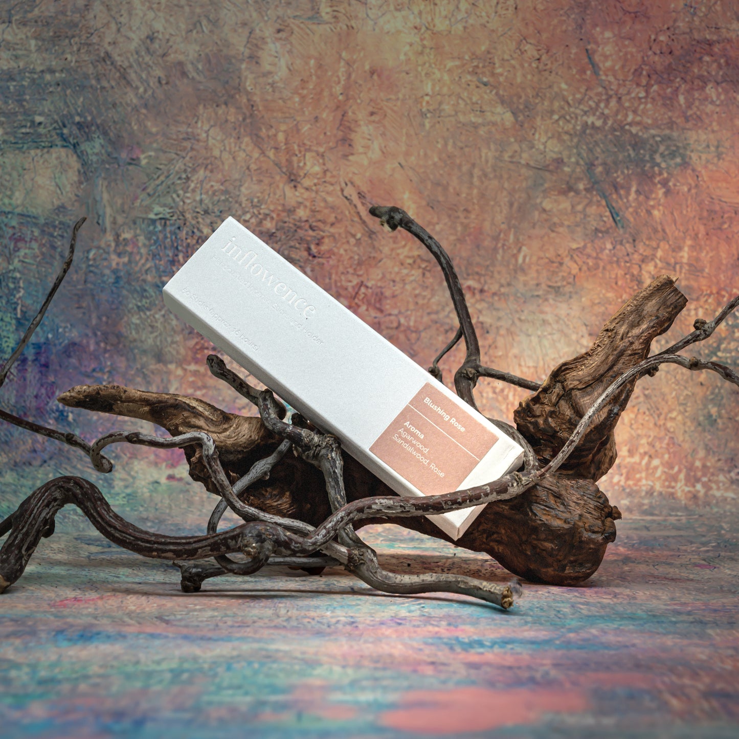 Blushing Rose incense box resting on natural wood with delicate branches, set against a Claude Monet–inspired canvas — a dreamy, floral scene evoking soft beauty and ritual calm.