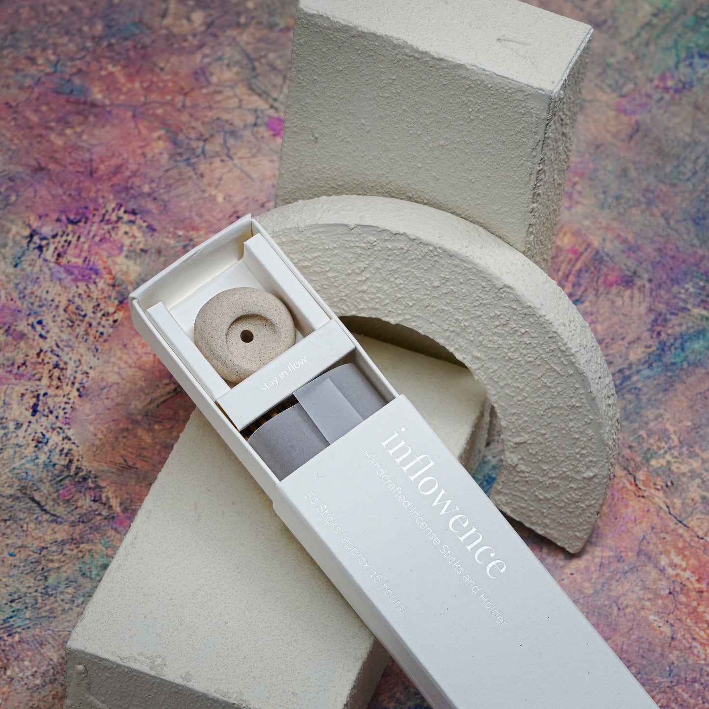 Close-up shot of an open incense box showcasing the packaging, incense sticks, and a clay incense holder, placed on a white textured block with a Claude Monet–inspired background — a dreamy, artistic, and serene atmosphere.