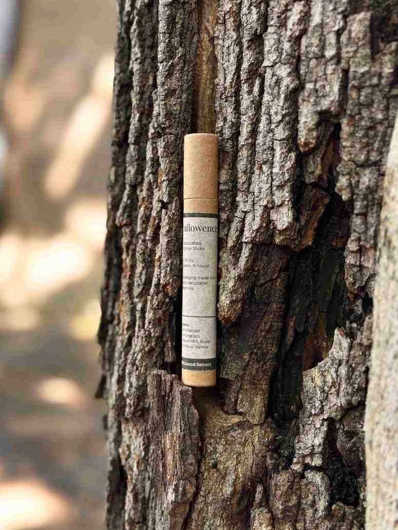 A cylindrical inflowence incense tube is propped against a tree trunk, representing a slow ritual and a way of creating space between tasks.