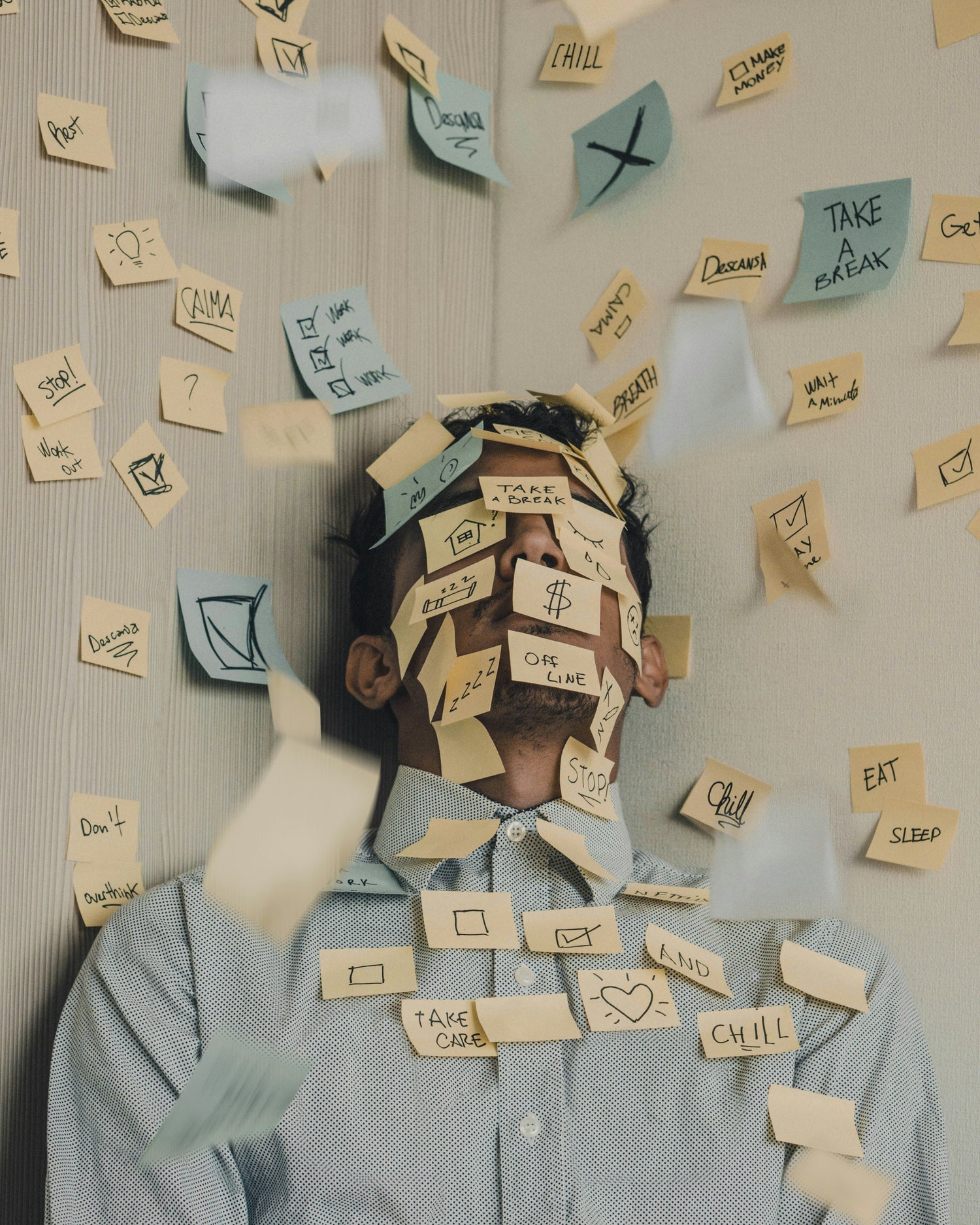 Man covered in sticky notes with phrases like ‘Take a break,’ ‘$,’ and ‘Sleep Work Eat’—illustrating stress, overwhelm, and the pressure of modern life.