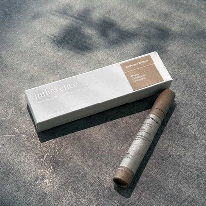 Inflowence Ambergris Whisper incense box and kraft paper tube displayed on a sunlit stone surface—featuring a blend of sandalwood and ambergris, crafted to support emotional reset through grounding scent rituals.
