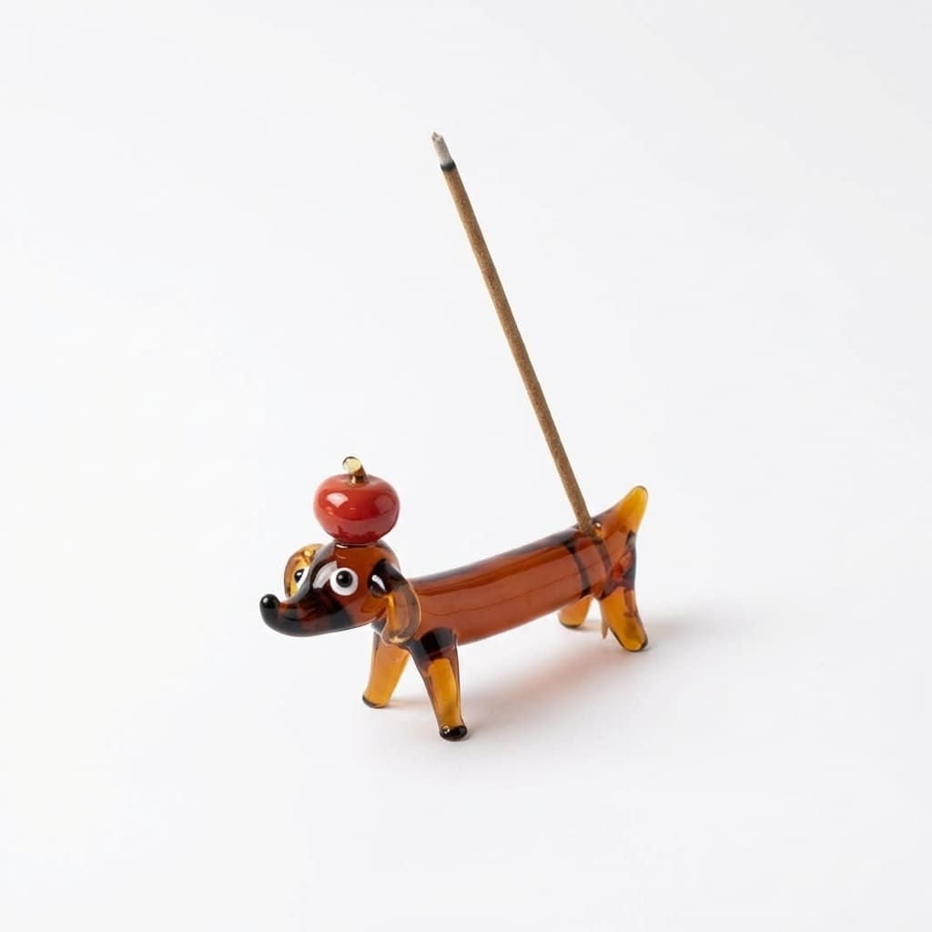 Apple Pup Incense Holder product shot on a clean white background, showing a hand-shaped glass incense holder crafted as a small amber dachshund with a red apple on its head and an incense stick placed in its back.