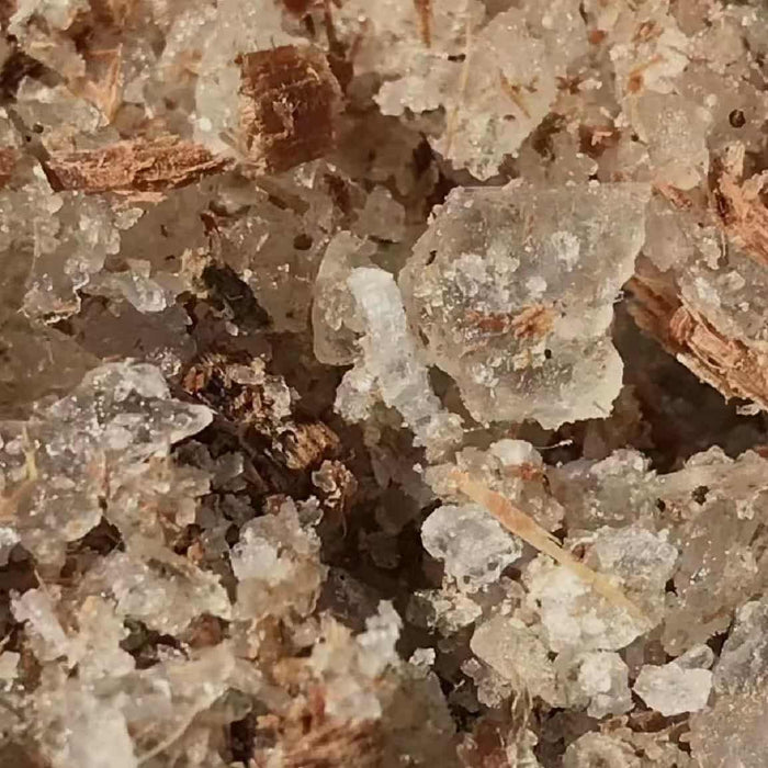 A close-up of translucent, crystal-like borneol pieces mixed with small, brown wood shavings. The texture and appearance suggest a scent that is cooling and camphor-like, soothing the senses while clearing the airways.