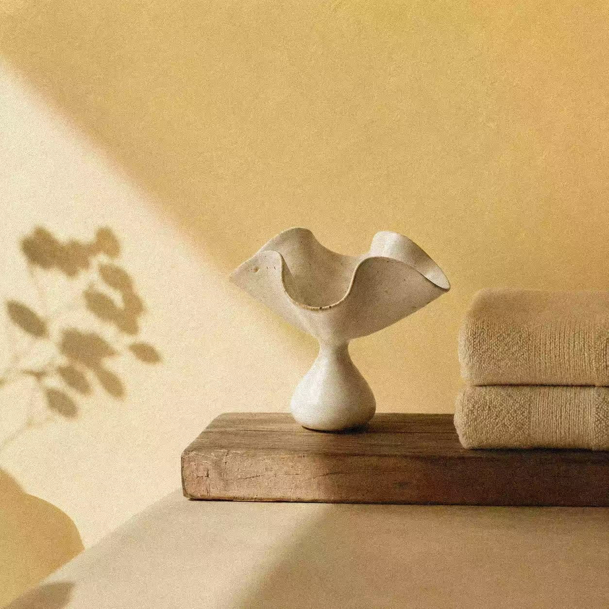 Ceramic incense holder shaped like an open petal, styled on a warm wooden shelf with folded towels, soft natural light, and a calm ritual setting for holding incense sticks and catching ash.
