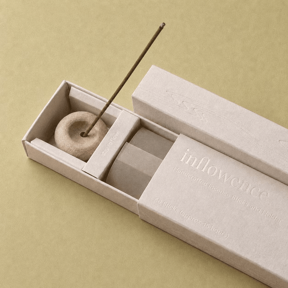 Close-up of an open inflowence incense box with a ceramic holder and a lit incense stick on a green background.