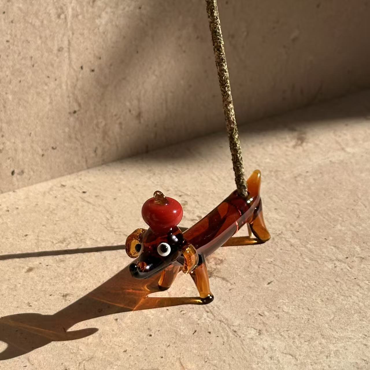 andcrafted glass incense holder shaped like a dachshund balancing an apple on its head, designed to hold incense sticks or stand as a decorative object