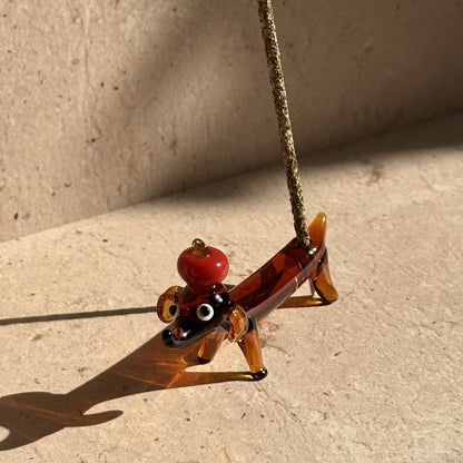 andcrafted glass incense holder shaped like a dachshund balancing an apple on its head, designed to hold incense sticks or stand as a decorative object
