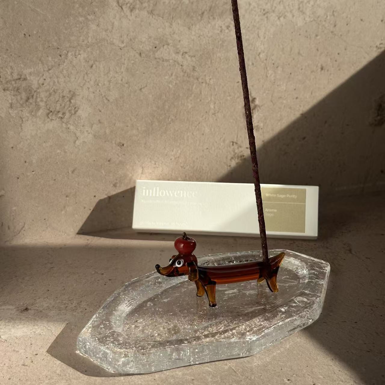 Apple dachshund glass incense holder placed on a handcrafted glass ash tray, holding a burning incense stick