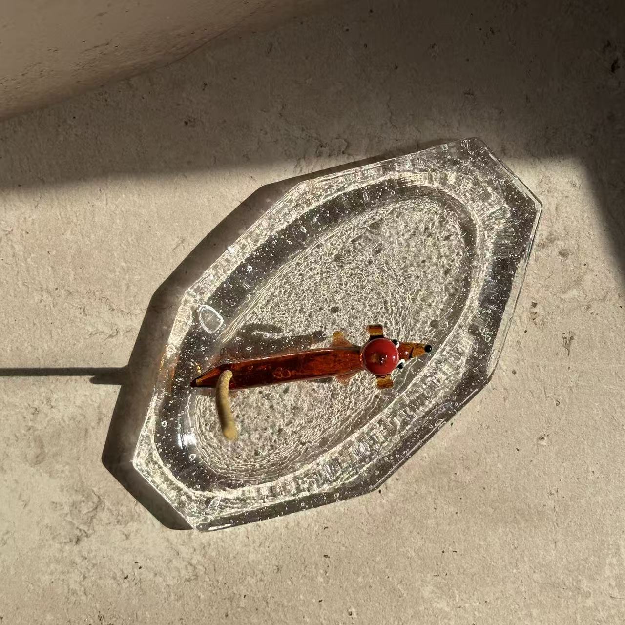 Apple dachshund glass incense holder placed on a handcrafted glass ash tray, holding a burning incense stick