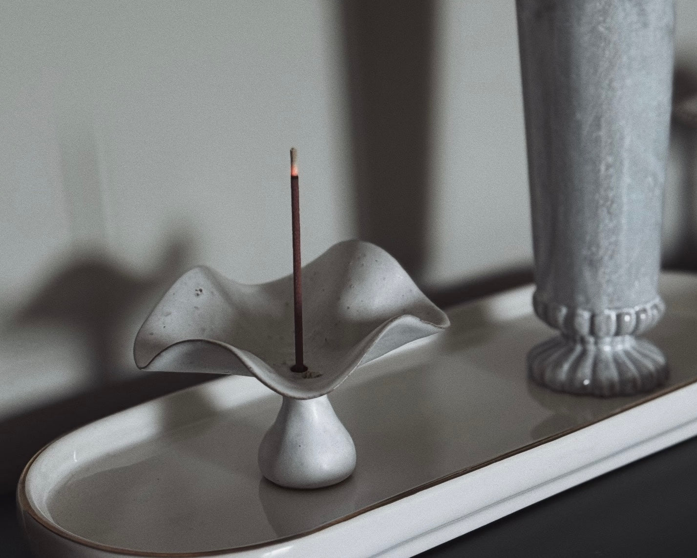 A ceramic incense holder holding a burning incense stick, creating a calm, minimalist ritual moment at home