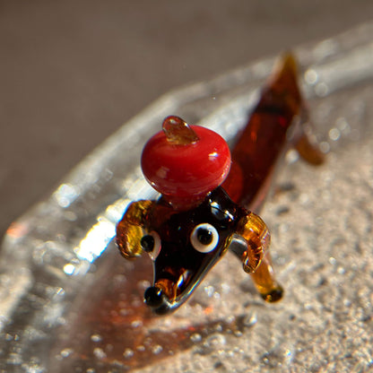 Close-up front view of a handcrafted glass apple dog incense holder, featuring a sculptural dog form with a red glass apple detail on top, placed on a clear glass ash catcher.