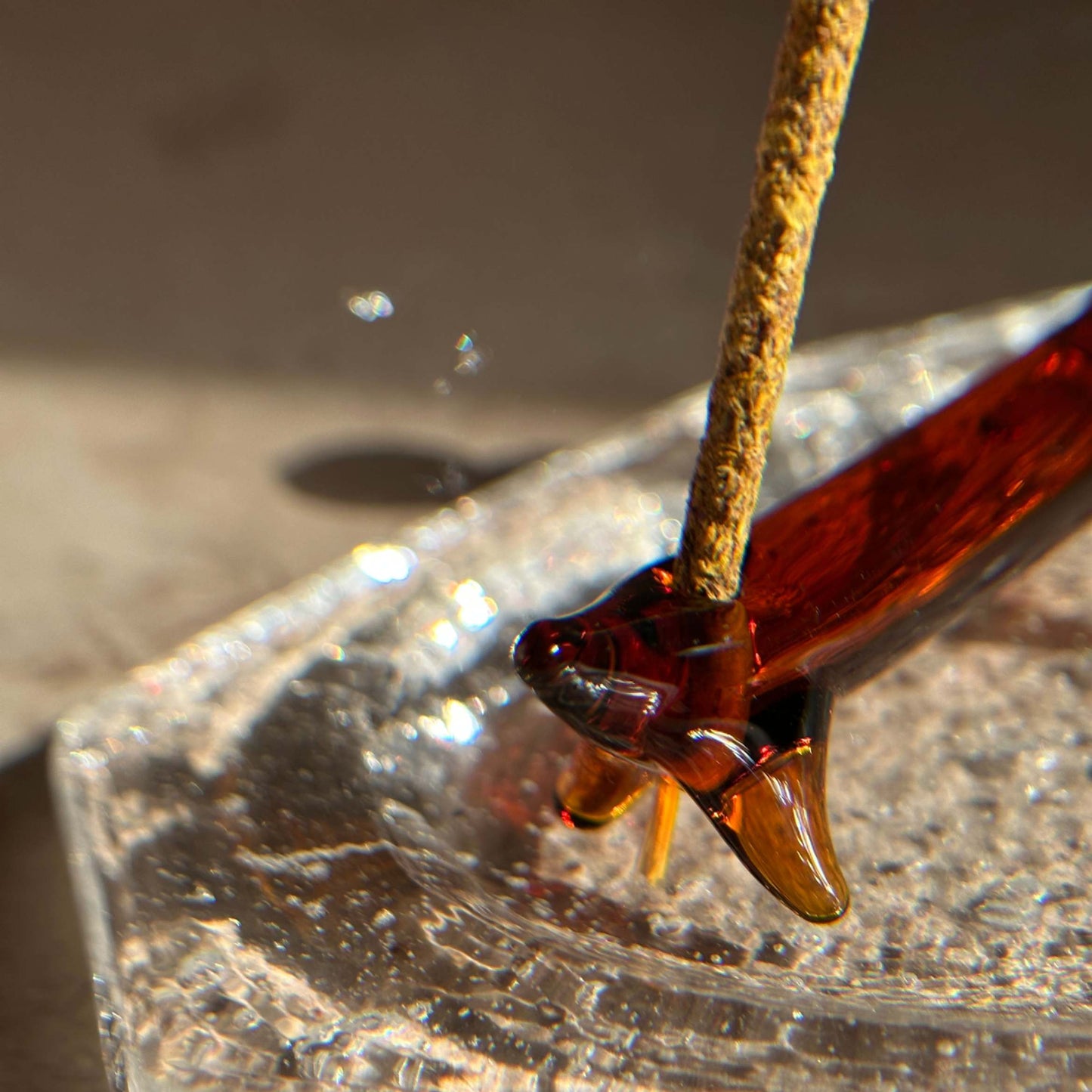 Close-up of a handcrafted apple dog incense holder with a bamboo incense stick inserted, placed on a clear glass ash catcher.