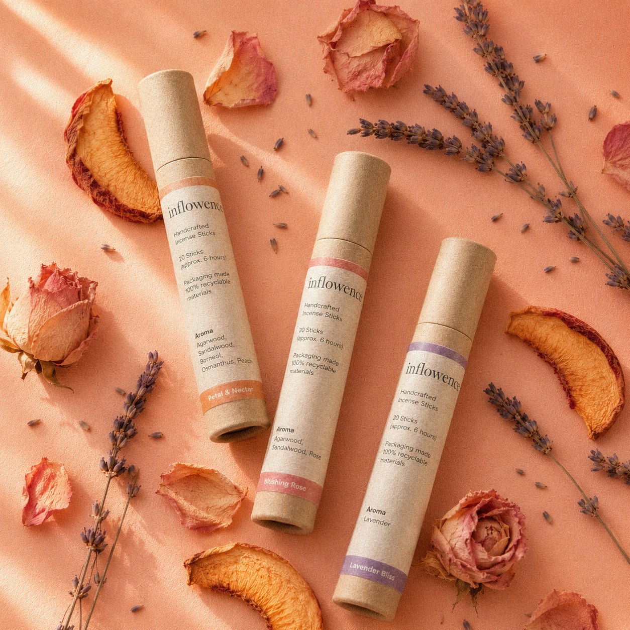 In Bloom Trio – Incense Set featuring Petal & Nectar flower incense, Blushing Rose rose incense, and Lavender Bliss lavender incense, arranged on a soft peach background with dried peach slices, lavender sprigs, dried roses, and scattered petals, designed to uplift the mood, soften stress, and bring light, refreshing floral rituals for busy minds.