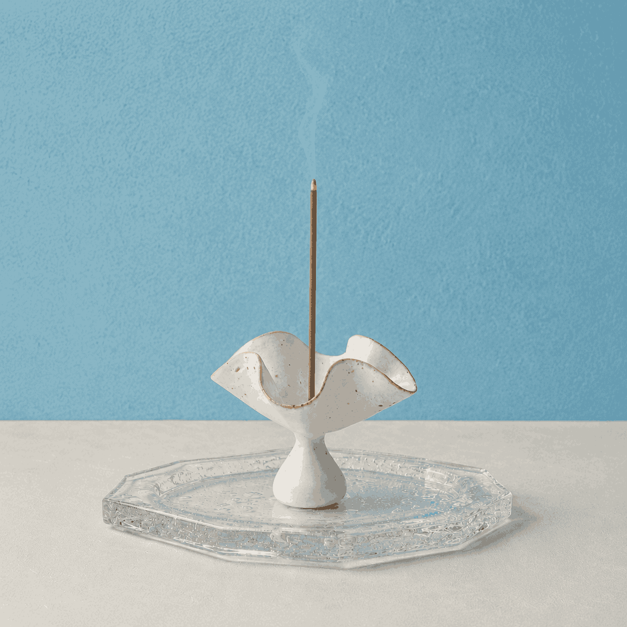 Kumo Glass Incense Tray paired with a ceramic petal incense holder and a burning incense stick, shown on a white surface against a blue background as a handcrafted glass tray designed to catch falling ash during use.