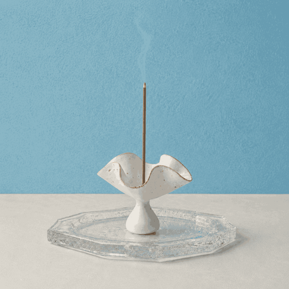 Kumo Glass Incense Tray paired with a ceramic petal incense holder and a burning incense stick, shown on a white surface against a blue background as a handcrafted glass tray designed to catch falling ash during use.