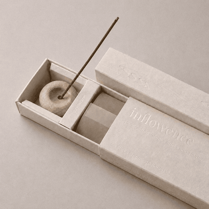 Close-up of an open inflowence incense box with a ceramic holder and a lit incense stick on a purple background.