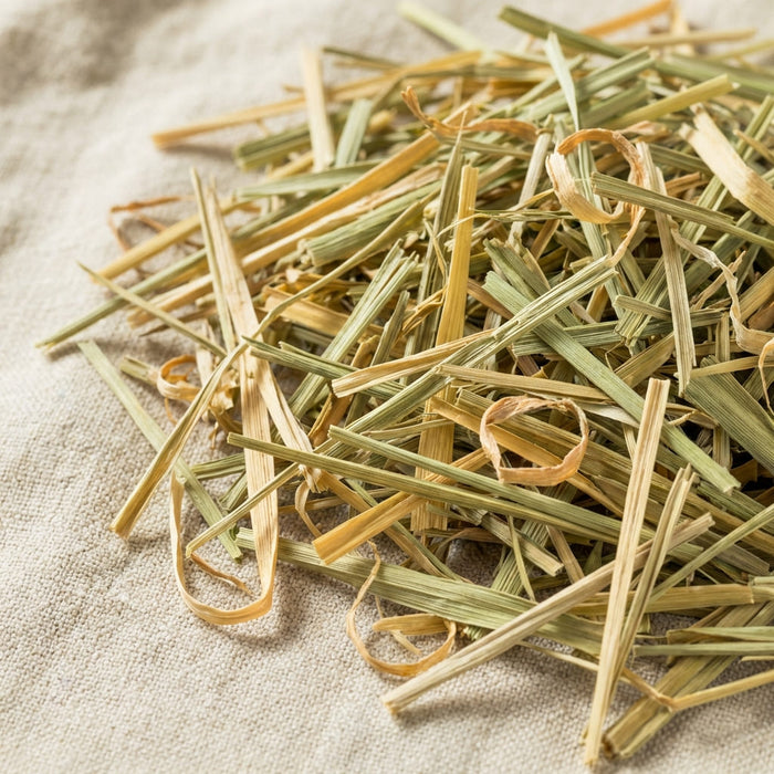 dried lemongrass cut into thin pale yellow strips gathered in a wooden bowl on a soft linen surface in natural light, a key ingredient used in inflowence patchouli incense named 'Wildwood Retreat'.