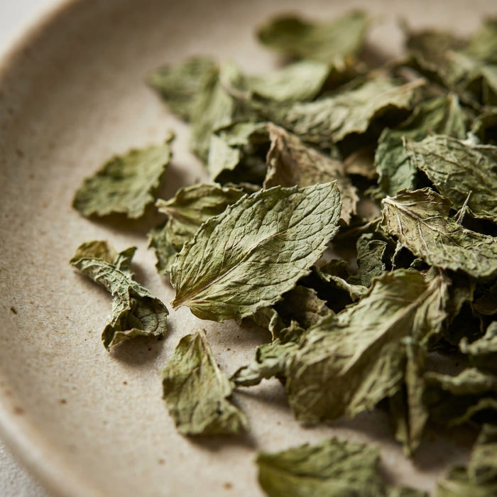 dried mint leaves with curled edges and muted green tones spread on a ceramic plate in soft natural light, a key ingredient used in inflowence Deep Dream lavender incense