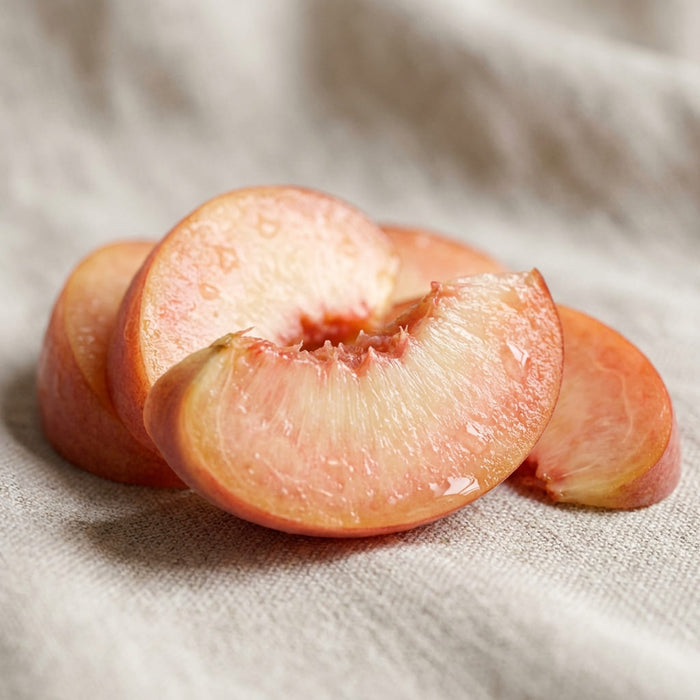 ripe peach sliced open with juicy flesh and soft golden-pink tones resting on a neutral linen surface in gentle natural light, a key ingredient used in inflowence flopwer incense named 'Petal & Nectar'.