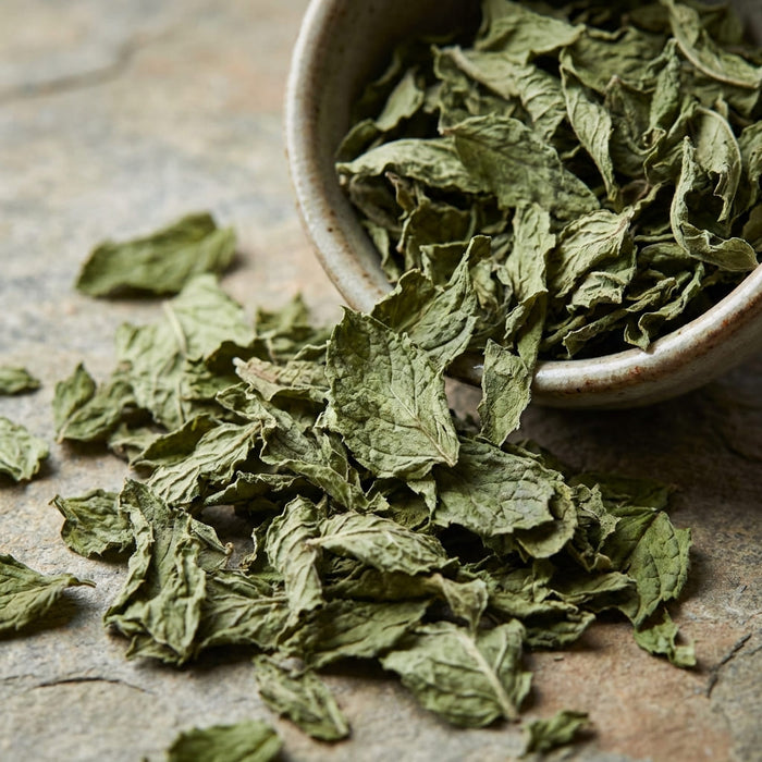 dried peppermint leaves with textured surface and deep green tones arranged on a rustic plate in soft natural light, a key ingredient used in inflowence patchouli incense named 'Wildwood Retreat'.