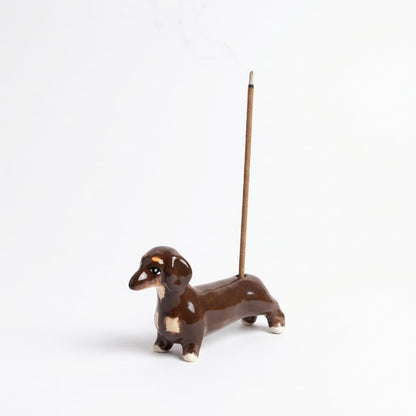 Sausage Dog Incense Holder product shot on a clean white background, featuring a compact hand-painted ceramic incense holder shaped like a dachshund with a lit incense stick placed in its back.
