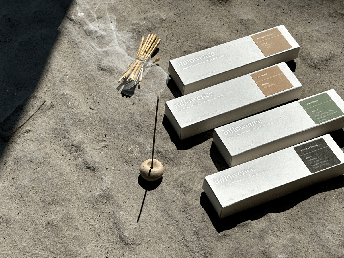  A close-up view of high quality incense from inflowence next to its packaging, highlighting the sleek design and a small wooden incense holder for the best smelling incense experience.