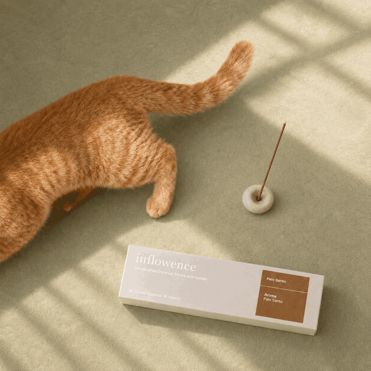 Top picks for cat households on the sensitive homes incense page, showing an orange cat walking past Inflowence Palo Santo incense, a small incense holder with a lit incense stick, and soft window light on a sage green background, curated for calm home rituals in pet-conscious spaces.
