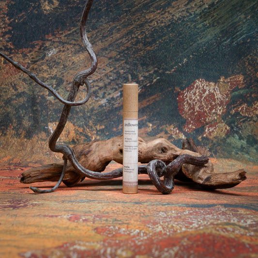 Ambergris Whisper incense tube styled with natural wood and branches, set against a green, red, and yellow oil painting–inspired backdrop — evoking a warm, earthy ritual atmosphere.