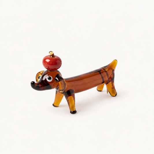 Apple Pup Incense Holder by Inflowence, a hand-shaped amber glass dachshund balancing a red apple on its head.