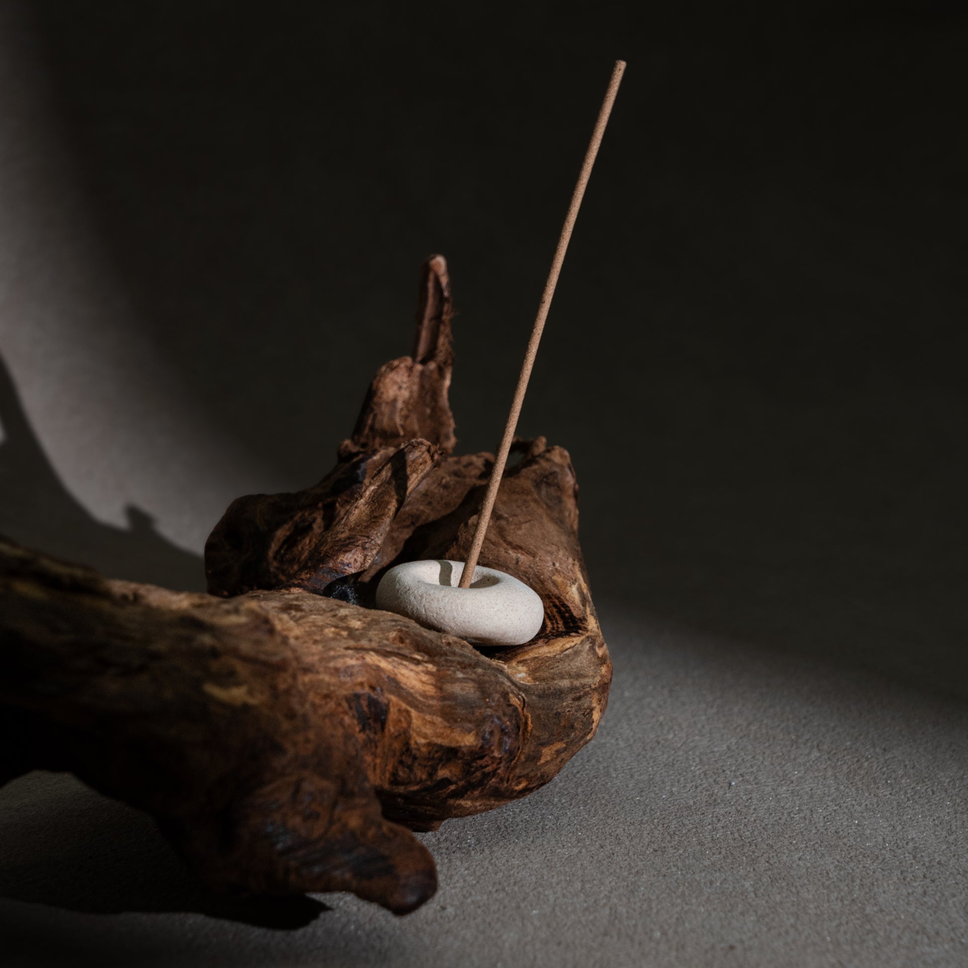 A handcrafted clay incense holder placed on natural wood, set against a beige-grey textured backdrop — a serene display of grounded ritual aesthetics.