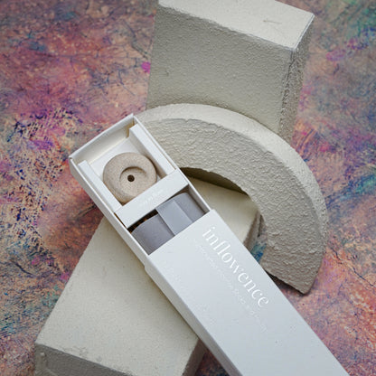 Close-up shot of an open incense box showcasing the packaging, incense sticks, and a clay incense holder, placed on a white textured block with a Claude Monet–inspired background — a dreamy, artistic, and serene atmosphere.