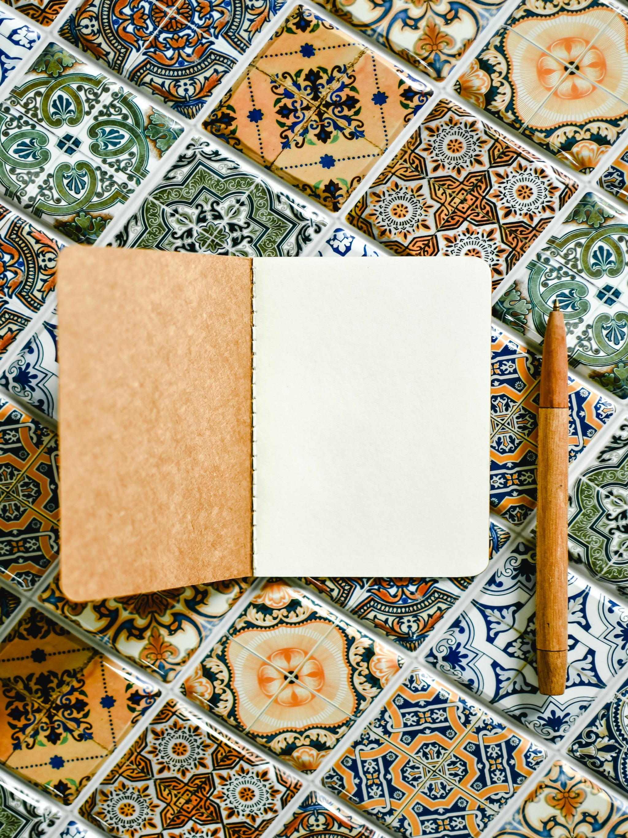 Blank journal with a wooden pen resting beside it on a patterned tile surface—inviting a moment of reflection, writing, or quiet intention.
