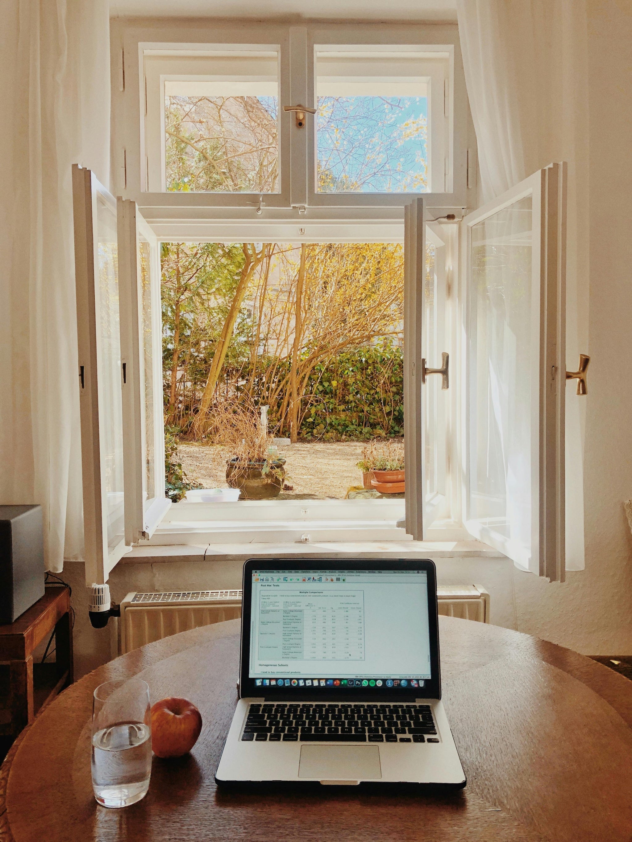 First-person view of a laptop on a desk near an open window with white curtains, looking out onto a lush green garden—evoking a sense of calm and mindful workspace.