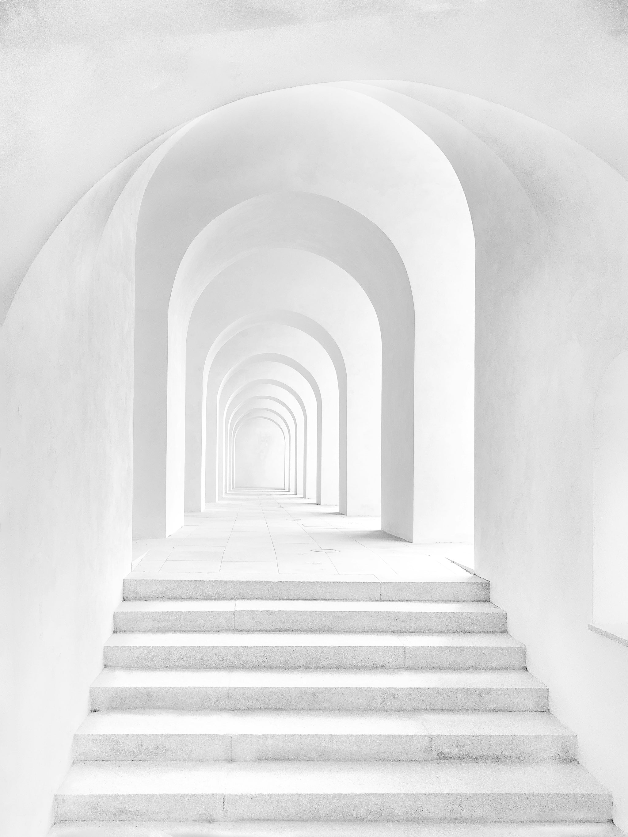 Minimalist white stone hallway with repeating arches, creating a soft visual rhythm and sense of depth—evoking serenity, clarity, and architectural flow.