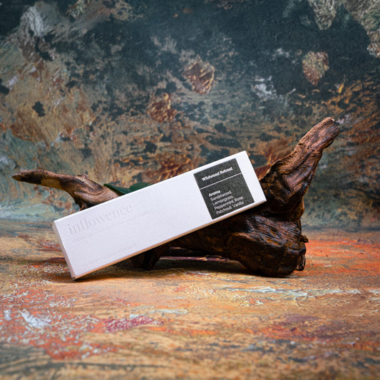 Wildwood Retreat incense box styled with natural wood and greenery, set against a green, red, and yellow oil painting–inspired backdrop — evoking a warm, earthy ritual atmosphere.